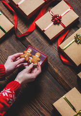 Female hands hold cookie near gift boxes over wooden table.
