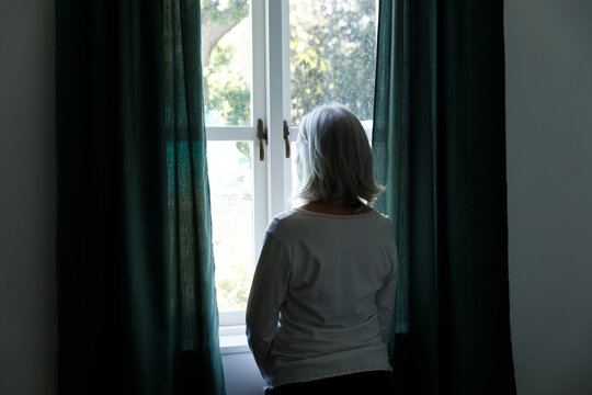 Rear view of senior caucasian woman looking out of window at home