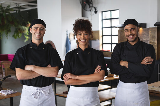 Portrait of diverse male and female chefs standing with hands crossed in restaurant kitchen