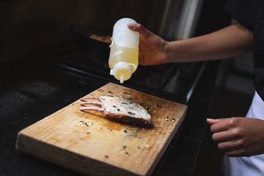 Mid section of chef adding olive oil over grilled ribs on wooden board