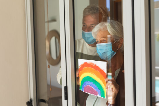 Senior caucasian couple wearing face masks holding rainbow picture