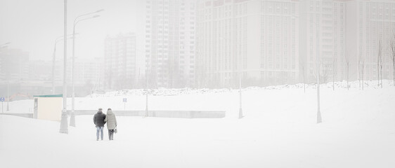 An adult couple walks through a snowy city. horizontal, Loneliness in a big city.