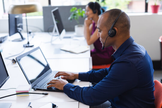 Mixed race man wearing phone headset in modern office, using computer