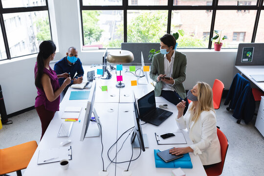 Diverse team wearing face masks brainstorming in creative office