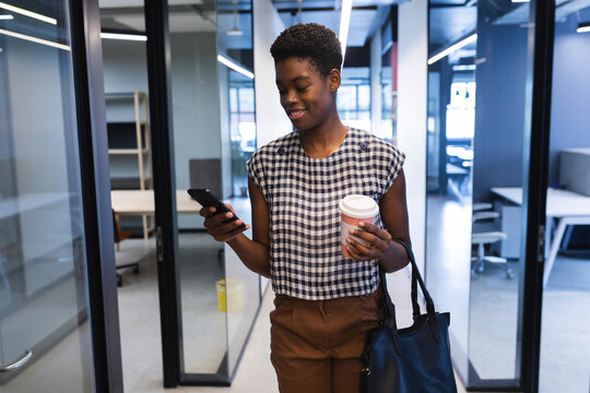 Smiling african american woman walking with smartphone in creative office