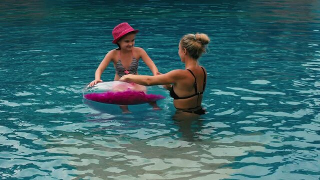 The mother with little daughter have fun in the pool. Mom plays with the child. The family enjoy summer vacation in a swimming pool jumping, spinning, splash water. Slow motion.