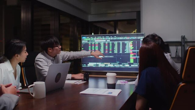 Young Asian businessman lead group of business financial team in strategic meeting presentation, work late night in office. Marketing strategy analysis, stock market trading, or corporate teamwork