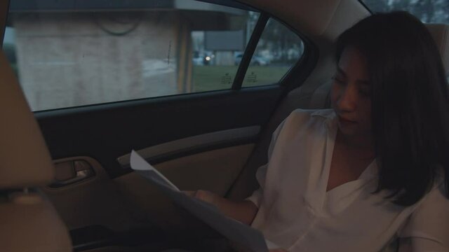 Successful young Asia businesswoman in fashion office clothes working in sitting back seat of car in urban modern city in the morning. Business on the go to work concept.