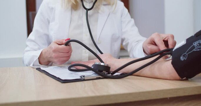 Close up of Caucasian female doctor hands measuring blood pressure of patient with medical manometer while sitting in cabinet in hospital at appointment. Medical tools. Healthcare concept