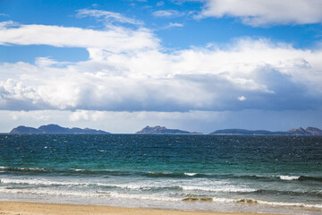 Fototapeta na wymiar Spain Vigo Praia do Vao beach water waves blue water sky clouds hills mountains Playa de Calzoa Punta elena Enseada de Samil