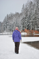 Woman standing near the almost frozen river by the red cliffs