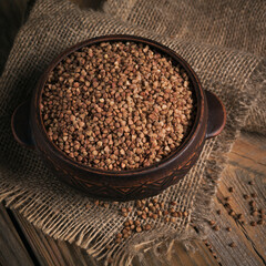 Organic uncooked scattered buckwheat grain in a bowl on a rustic wooden background. Healthy and diet food concept.