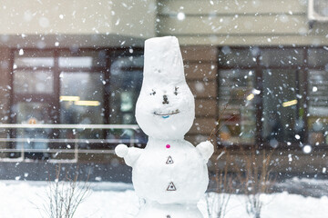 Big white smiling frozen alone snowman stand on city street at snowstorm blizzard against apartment...