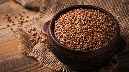 Organic uncooked scattered buckwheat grain in a bowl on a rustic wooden background. Healthy and diet food concept.