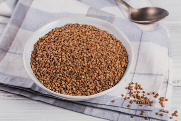 Bowl of dry raw buckwheat groats on a white wooden background. Cooking buckwheat porridge concept.
