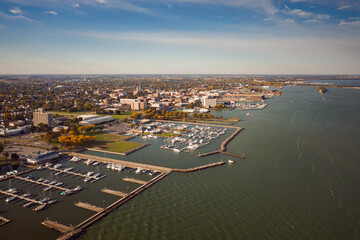 Incredible aerial city skyline panorama photograph of Sandusky, Ohio from the shoreline of the bay in Lake Erie with parks and harbors seen below on a sunny day.