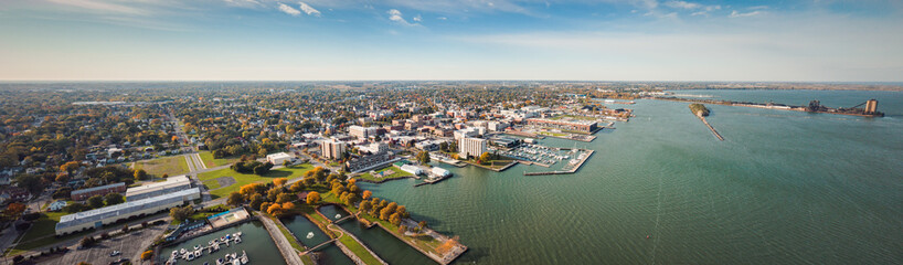 Incredible aerial city skyline panorama photograph of Sandusky, Ohio from the shoreline of the bay in Lake Erie with parks and harbors seen below on a sunny day.