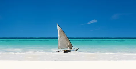 Wall murals Zanzibar An Exotic Sail Boat Sits On White Sand In The Tropics