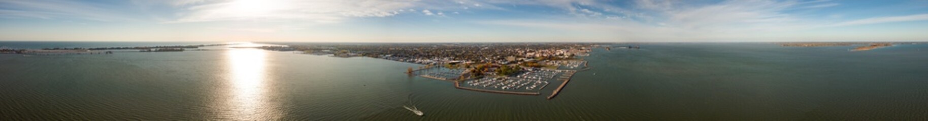Incredible aerial city skyline wide angle panorama photograph of Sandusky, Ohio from the shoreline of the bay in Lake Erie with parks and harbors seen below on a sunny day as a boat passes by.