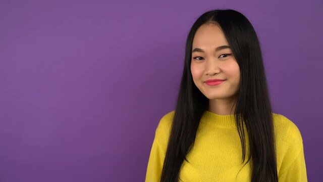 smiling young asian woman on isolated purple background shows index finger. Free space for object or text 4K