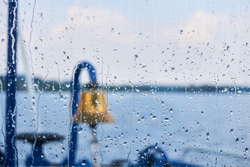 background - raindrops on the glass of the wheelhouse, behind which one can guess a blurred details of the ship and a rainy waterscape © Evgeny