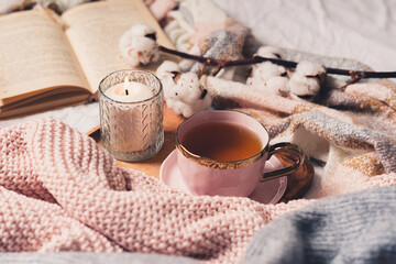 Details of still life in the home interior of living room. Sweater, cup of tea, cotton, cozy, book, candle. Moody. Cosy autumn winter concept. Decoration, vintage with glow bokeh.