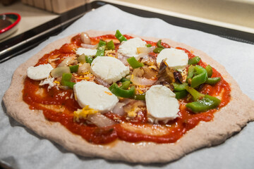 Homemade fresh italian pizza dough with mozarella, green peppers, oregano, french cheese and marinara sauce. Ready to be baked in the pizza oven.