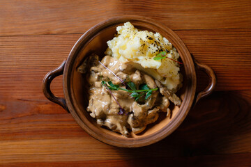 Fried meat with mushrooms and potatoes in a clay plate close-up.