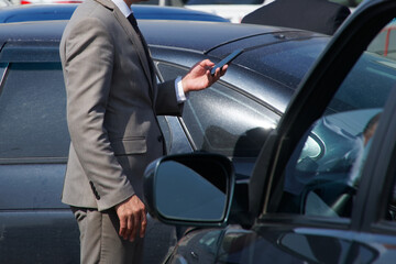 A man in a business suit - an official or a businessman talking on a smartphone among black cars. Business meeting or conversation. Solving problems and tasks