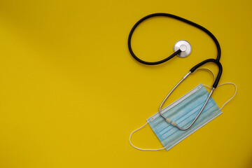 stethoscope and surgical mask top view on yellow background