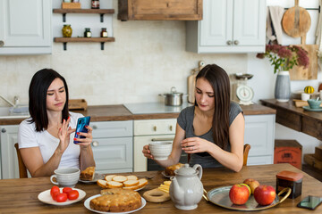 Two girls are drinking tea with cake and sweets at the table.