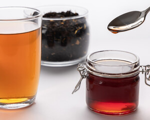 Tea concept, black tea leaves, tea drink in glass cup and honey in jar on the table, golden honey in spoon