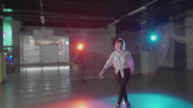 Group of teenage girls roller-skating in dark studio. Millennials rehearse trick moves practicing freeskating style. Young females trying new extreme nightlife lifestyle. Concept of youth, pop culture