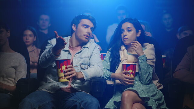 Upset man speaking in movie theater. Frustrated couple eating in cinema.
