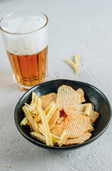 Beer glass and potato chips in a black bowl on concrete background - snack bar or pub menu