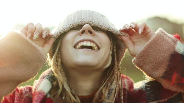 Cheerful woman smiling and covering eyes with knit hat while standing outdoors