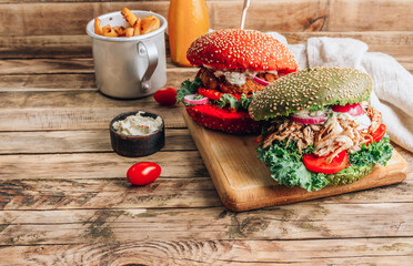 Homemade various chicken burger with colorful buns, kale, red onion, tomato and mayonnaise sauce served on wooden board. Wooden rustic background. Selective focus