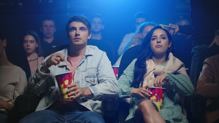Young couple eating popcorn in cinema. Angry man getting irritated indoor.