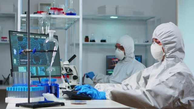 Scientists in protection suits working in chemical equipped laboratory. Team of biologists examining vaccine evolution using high tech and technology researching treatment against covid19 virus