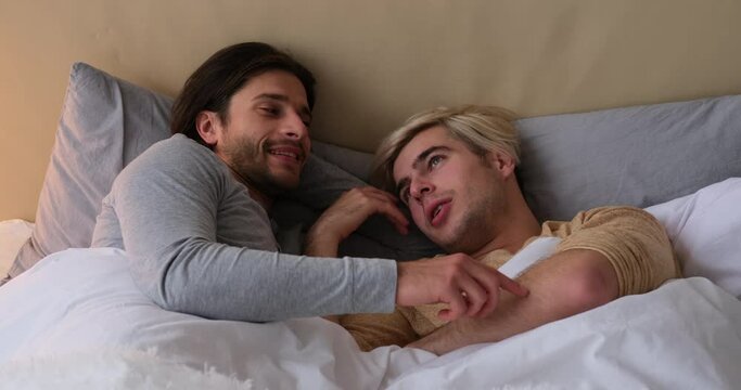 Loving gay couple talking and spending time together in bed