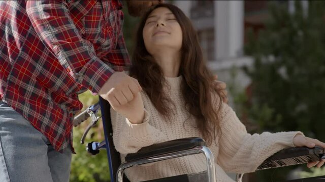 Portrait of disabled happy young woman n wheelchair and her husband kissing her. Asian handicapped girl with paralysis living full life. Couple in love. 6k downscale 10 bit color.