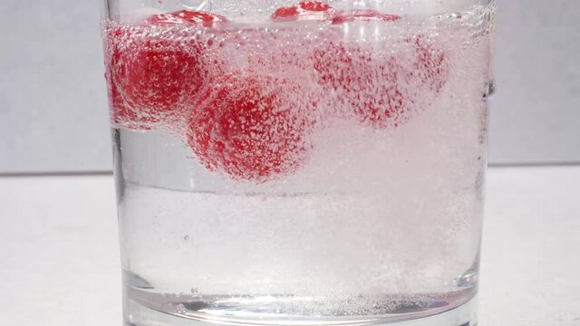 Raspberries being dropped into clear seltzer water