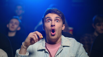 Shocked man watching horror film in cinema. Scared guy eating popcorn in movie