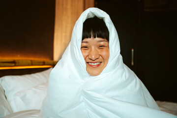 Short hair woman playing with white blanket in bedroom.