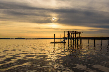 Obraz premium Cloudy Golden Sunset Sunrise on a River with a Dockhouse and Perched Birds in Silhouette 