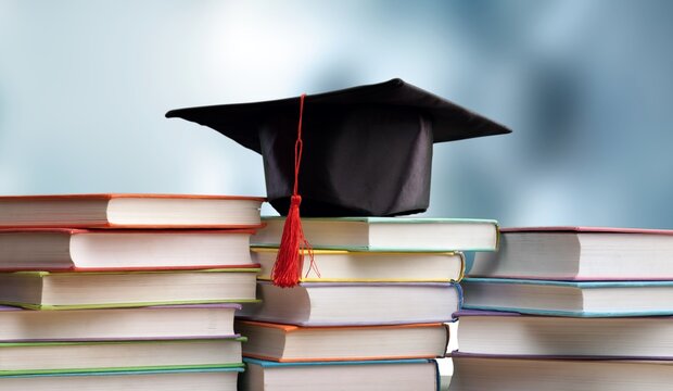 Stack school books with black graduation hat