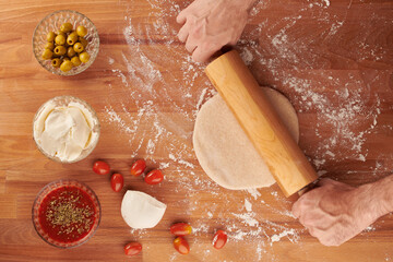 Making italian pizza step by step: small dough rolled out with a rolling pin