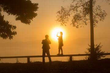Fototapeta na wymiar Silhouette young couple enjoying the sunrise in the mountain sea mist in Thailand.