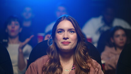 Amazed woman applauding at movie premiere. Smiling girl enjoying film in cinema.