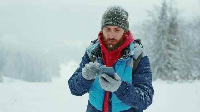 Portrait young man outdoor in winter snowy forest using smartphone for message. Online christmas greetings. Vacation technology cold holiday travel snow. Slow motion